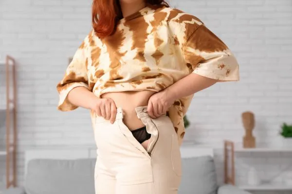 Image of woman trying to do her trousers up after pregnancy weight gain Bradford